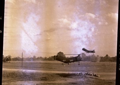 An Army helicopter is hovering above the ground as other helicopters are seen in the background.