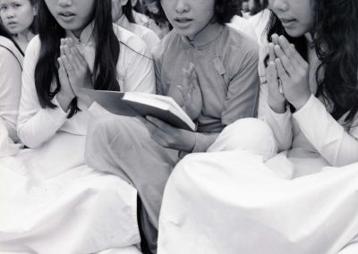 Three women are seen praying, the woman in the middle is holding some type of book